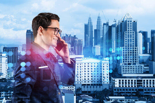 A young handsome eastern businessman processing conference call to develop social media marketing strategy to achieve business goals. Hologram icons over Kuala Lumpur background.