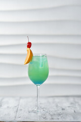 green cocktail in a glass with orange and cherry on a skewer