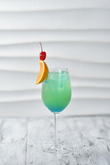 green cocktail in a glass with orange and cherry on a skewer