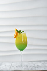 green cocktail in a glass with orange and cherry on a skewer