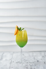 green cocktail in a glass with orange and cherry on a skewer