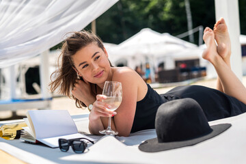 young woman in black dress spending summer time and relaxing in four-poster bed near beach
