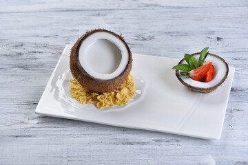 Obraz na płótnie Canvas coconut dessert in coconut with pulp, corn flakes and strawberries on a white square plate, pina colada