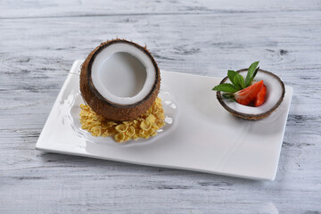 coconut dessert in coconut with pulp, corn flakes and strawberries on a white square plate, pina colada