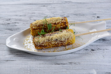 grilled corn on the cob with parmesan cheese and sprouts on a white fish-shaped plate