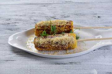 grilled corn on the cob with parmesan cheese and sprouts on a white fish-shaped plate