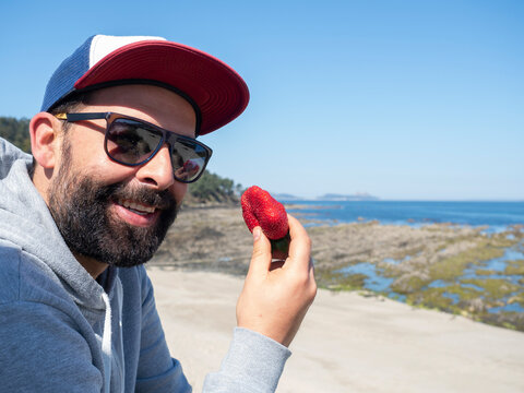 smiling man looking at camera and eating a strawberry
