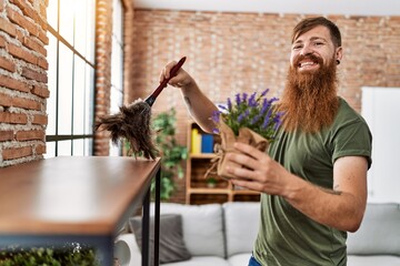 Young redhead man cleaning dust and holding lavender plant at home
