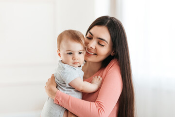 Mother and baby. Young happy mother holding infant child in arms, mom cuddling with her kid and smiling