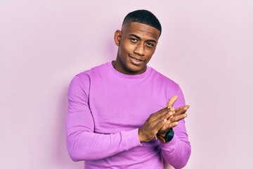 Young black man wearing casual pink sweater clapping and applauding happy and joyful, smiling proud...