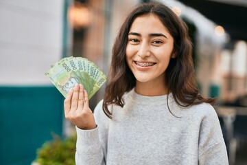 Young middle east girl smiling happy holding chile pesos banknotes at the city.