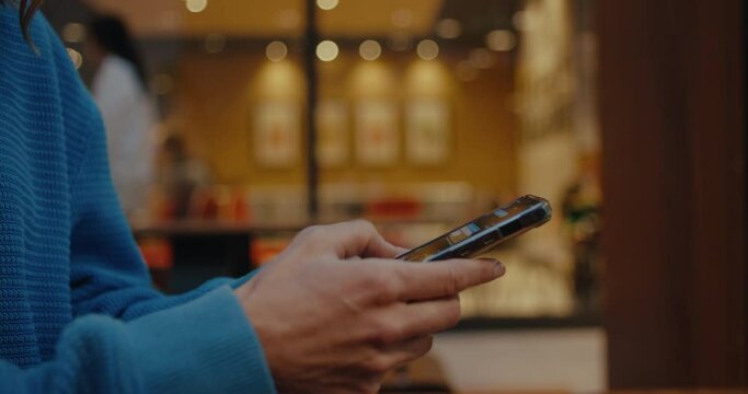 Close up profile side view on young woman, teen hands holding mobile phone, using smartphone, typing message, chatting with friends on social media, sitting outdoors in city cafe on weekend, day off