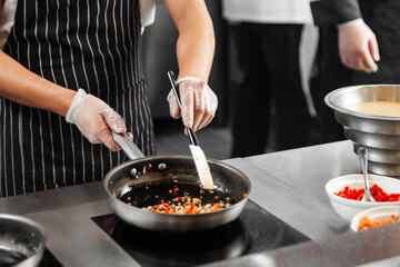 Chef in restaurant kitchen cooking vegetables on a frying pan