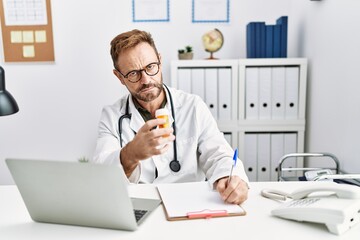 Middle age hispanic man wearing doctor uniform holding pills at clinic