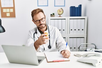 Fototapeta premium Middle age hispanic man wearing doctor uniform holding pills at clinic