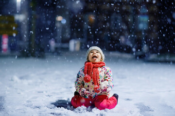 Adorable little toddler girl walking outdoors in winter. Cute toddler during strong snowfall on...