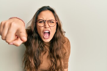 Young hispanic girl wearing casual clothes and glasses pointing displeased and frustrated to the...