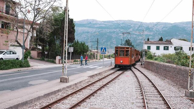 Tourists looking at famous tram moving on railroad tracks. Traditional historic train traveling through the old town of Soller in Palma De Mallorca in Spain.