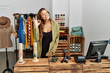 Beautiful hispanic woman working at fashion shop smiling positive doing ok sign with hand and fingers. successful expression.