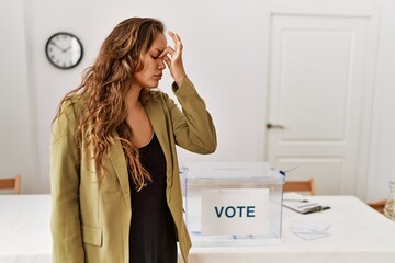 Beautiful hispanic woman standing at political campaign room tired rubbing nose and eyes feeling...