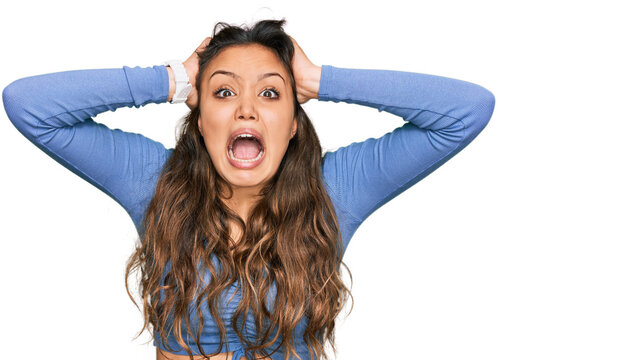 Young hispanic girl wearing casual clothes crazy and scared with hands on head, afraid and surprised of shock with open mouth