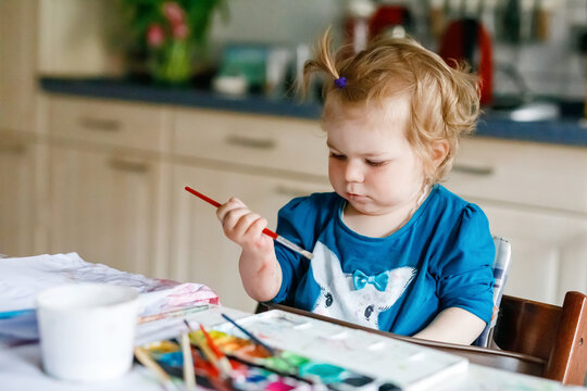 Cute happy little girl painting with water color on paper. Baby child learning different skills, creative leisure and activity for small children.