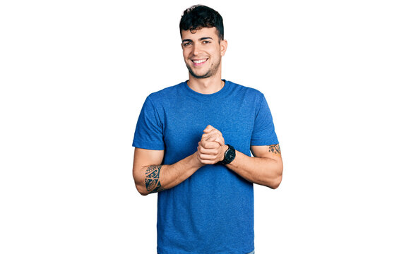 Young hispanic man wearing casual t shirt with hands together and crossed fingers smiling relaxed and cheerful. success and optimistic