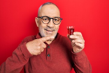 Handsome mature man drinking whiskey shot smiling happy pointing with hand and finger