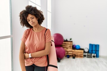 Obraz na płótnie Canvas African american woman with afro hair holding yoga mat at pilates room looking sleepy and tired, exhausted for fatigue and hangover, lazy eyes in the morning.