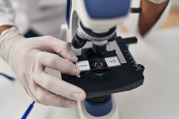 Young hispanic man wearing scientist uniform using microscope at laboratory