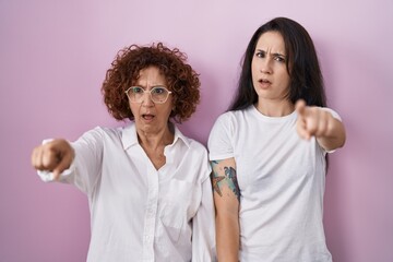 Hispanic mother and daughter wearing casual white t shirt over pink background pointing displeased and frustrated to the camera, angry and furious with you