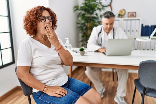 Senior woman sitting at doctor appointment bored yawning tired covering mouth with hand. restless and sleepiness.