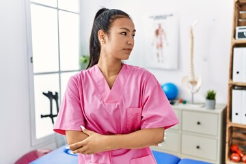Young hispanic woman working at pain recovery clinic looking to side, relax profile pose with natural face with confident smile.