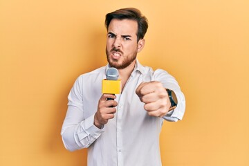 Handsome caucasian man with beard holding reporter microphone annoyed and frustrated shouting with...