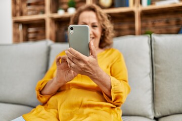 Middle age caucasian woman usin smartphone sitting on the sofa at home.