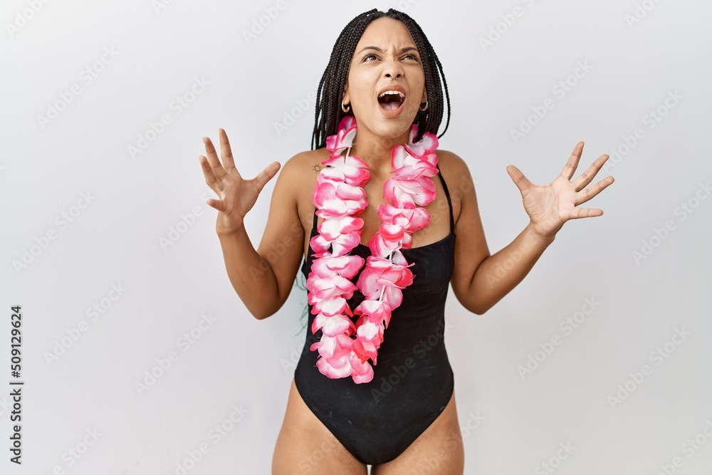 Poster Young african american woman wearing swimsuit and hawaiian lei crazy and mad shouting and yelling with aggressive expression and arms raised. frustration concept.