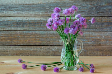 Bouquet of purple flowers of decorative onions in a glass vase on a wooden background