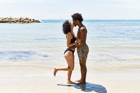 Young interracial tourist couple wearing swimwear kissing and hugging at the beach.