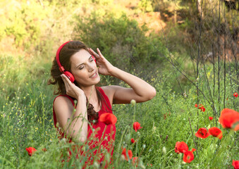 portrait of a beautiful young woman with closed eyes sitting in a field of poppies listening to music on her headphones