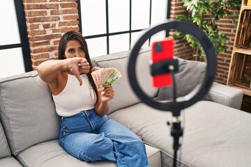 Young hispanic woman recording tutorial with smartphone at home with angry face, negative sign showing dislike with thumbs down, rejection concept