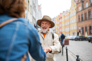 Fototapeta premium Happy senior man giving hand to senior woman, couple in love holding outdoors in town