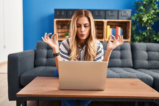Young blonde woman having online yoga class sitting on sofa at home