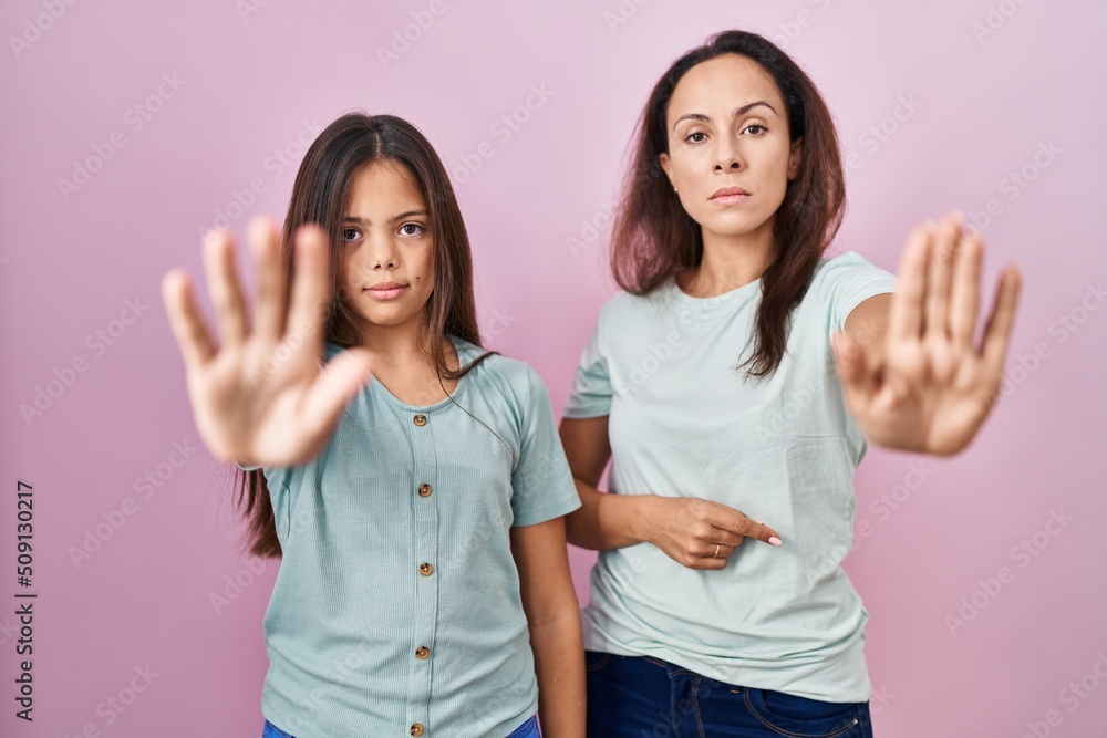 Canvas Prints Young mother and daughter standing over pink background doing stop sing with palm of the hand. warning expression with negative and serious gesture on the face.