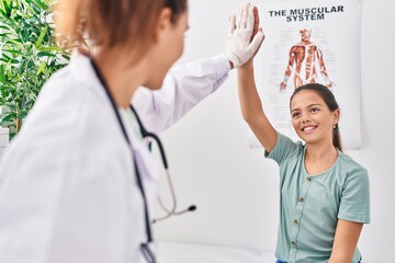 Woman and girl doctor and patient high five with hands raised up at clinic