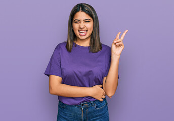 Young hispanic girl wearing casual purple t shirt smiling with happy face winking at the camera...