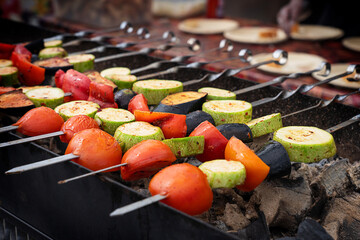 Hot organic healthy skewered vegetables such as sliced tomato, zucchini and eggplant being grilled or roasted on skewers on outdoor barbeque grill at restaurant for summer picnic as vegetarian food