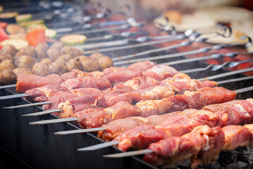 Selective focus on raw pork marinated vinegar-pickled meat with spices being cooked on skewers on outdoor wood-fired barbeque grill for summer picnic at outside kitchen of restaurant for dinner