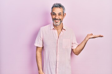 Handsome middle age man with grey hair wearing casual shirt smiling cheerful presenting and pointing with palm of hand looking at the camera.