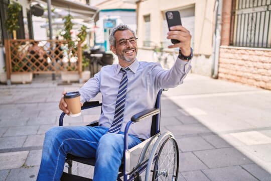 Middle age hispanic man sitting on wheelchair makes selfie by the smartphone at street