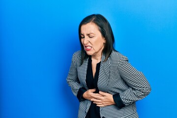 Middle age hispanic woman wearing business clothes with hand on stomach because nausea, painful disease feeling unwell. ache concept.